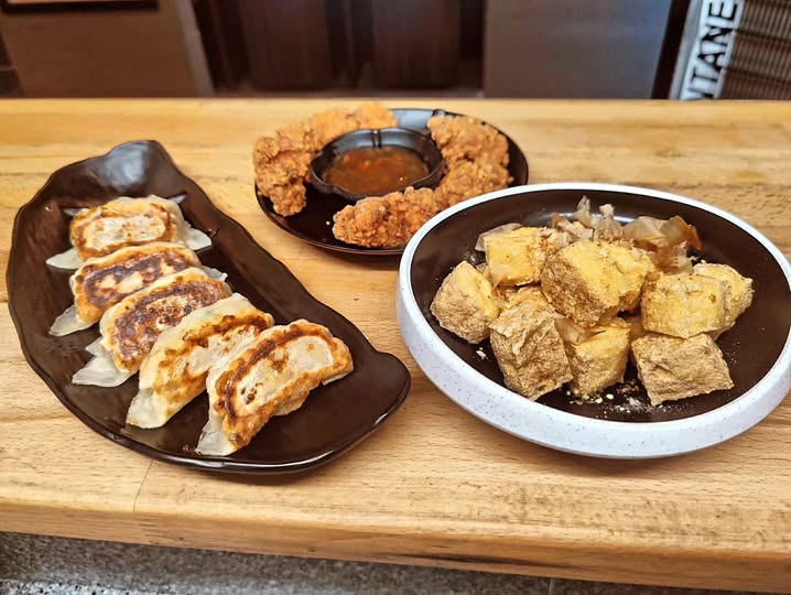 Gyoza, sprød karaage med dyppesauce og stegt tofu serveret på mørke fade